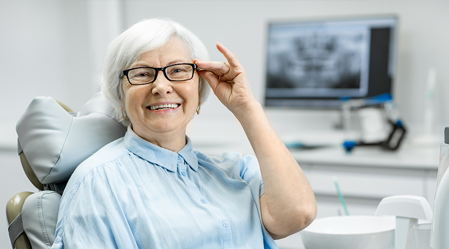 Elderly lady wearing glasses smiling at dentist
